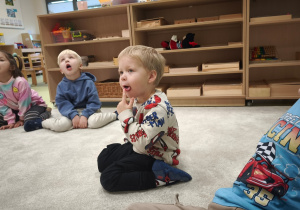 Chłopiec dotyka czubek języka palcem, dziewczynka zakrywa zęby górne językiem.