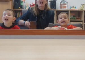 Chłpocy wykonują z logopedą zdania przed lustrem.