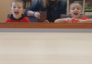 Chłopiec, logopeda i drugi chłopiec unosząc język, robią ćwiczenie o nazwie miseczka