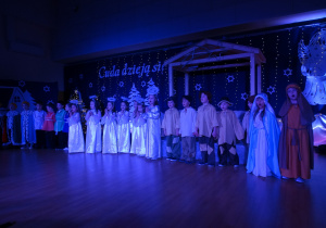 Dzieci w strojach stoją na scenie i śpiewają pastorałkę