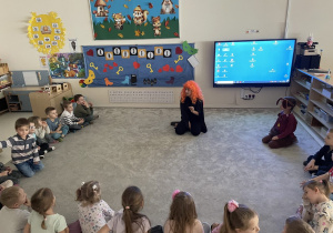 Pani w przebraniu wróżki opowiada dzieciom o Andrzejkach.