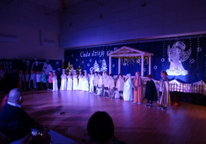 Dzieci na scenie w strojach jasełkowych śpiewają piosenkę