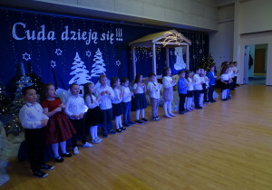 Dzieci w strojach galowych śpiewają piosenkę dla dziadków