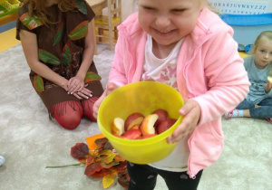 Pomocnica Pola częstuje dzieci jabłuszkami.