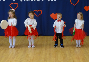 Czworo dzieci stoi w rzędzie z instrumentami i ozdobnymi wstążkami.