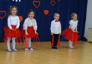Dzieci stoją w rzędzie z rękami opuszczonymi, przygotowane do kolejnej części występu.