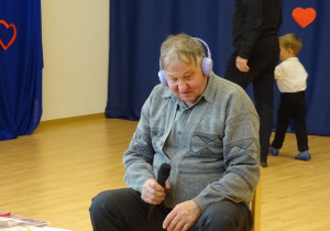 Starszy mężczyzna siedzi z mikrofonem w ręku.