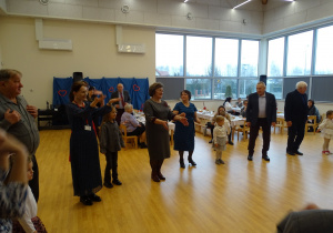 Dorośli i dzieci tańczą razem w sali.