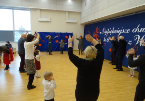 Dzieci i dorośli stoją w kręgu z uniesionymi rękami.