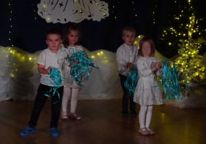 Dzieci stoją na scenie z niebieskimi wstążkami.