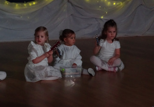 Dzieci siedzą i grają na instrumentach.