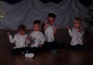 Chłopcy siedzą i trzymają małe instrumenty.