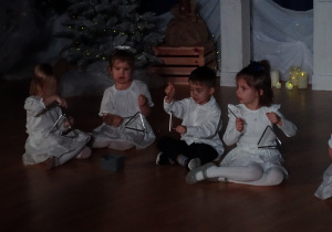 Dzieci siedzą i grają na trójkątach.