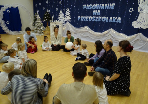 Dzieci i dorośli siedzą w kręgu na podłodze.