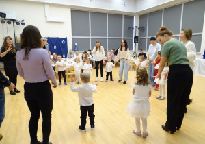 Dzieci i dorośli stoją w kręgu podczas zabawy.