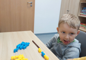 Chłopiec oblizuje usta, przed nim ustawione zwierzęta w kolorach żółtym i niebieskim