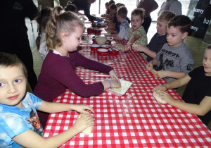 Dzieci obtaczają ciasto w mące