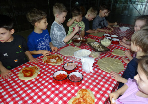 Dzieci układają ulubione dodatki na pizze, smarują sosem