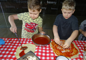 Dzieci układają ulubione dodatki na pizze, smarują sosem