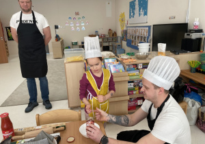 Dzieci pod okiem rodziców przygotowują sos pomidorowy.