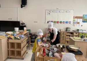 Dzieci pod okiem rodziców przygotowują sos pomidorowy.