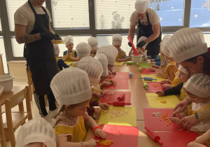 Dzieci kroją składniki do pizzy.