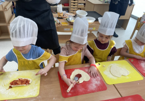 Dzieci smarują ciasto sosem pomidorowym.