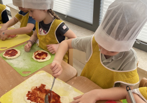 Dzieci smarują ciasto sosem pomidorowym.