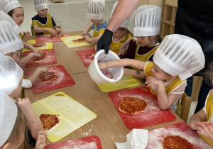 Dzieci kładą szynkę na pizzę.