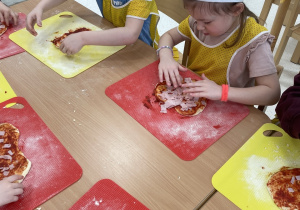 Dzieci kładą szynkę na pizzę.