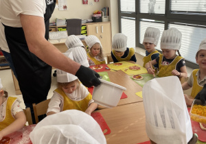 Tata Stasia rozdaje dzieciom składniki do pizzy.