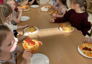 Dzieci jedzą pyszną pizzę.