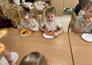 Dzieci jedzą pyszną pizzę.
