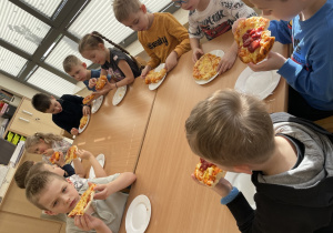 Dzieci jedzą pyszną pizzę.