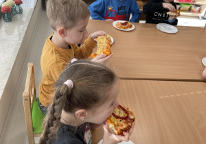 Dzieci jedzą pyszną pizzę.
