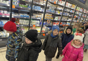 Dzieci oglądają jakie produkty przechowywane są w sklepowych lodówkach.