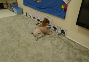 Dziewczynka dopasowuje sylwetę dinozaura do obrazka.