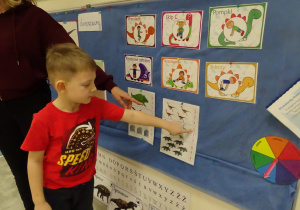 Chłopiec liczy dinozaury i wskazuje odpowiednią cyfrę.