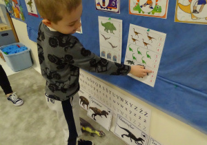 Chłopiec liczy dinozaury i wskazuje odpowiednią cyfrę.