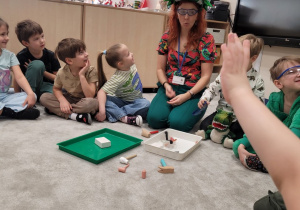 Pani w okularach ochronnych pokazuje dzieciom zestaw paleontologa