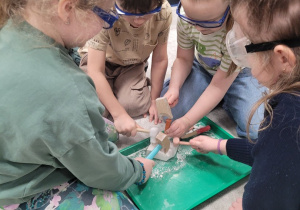 Dzieci w ochronnych okularach rozbijają skamielinę