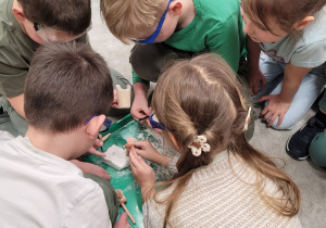 Dzieci w ochronnych okularach rozbijają skamielinę