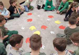 Dzieci siedzą w kole, w środku ślady dinozaurów