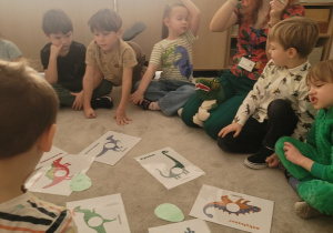 Pani prześwietla latarka jajo i ukazuje się w nim mały dinozaur