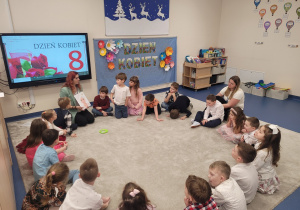 Dzieci siedzą w kole, pani pokazuje zadanie