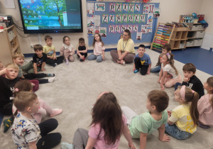 Dzieci siedzą w kole, w tle tablica z napisem dzień zespołu downa