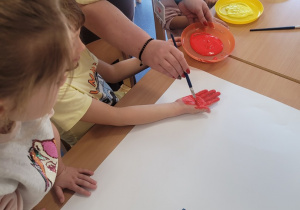 Dzieci odbijają umoczona w farbie rączkę wokół hasła na plakacie