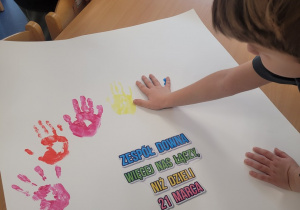 Dzieci odbijają umoczona w farbie rączkę wokół hasła na plakacie