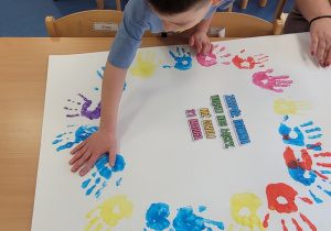 Dzieci odbijają umoczona w farbie rączkę wokół hasła na plakacie