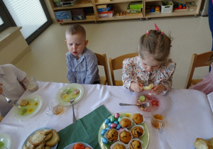 dzieci siedzą przy stole i jedzą śniadanie wielkanocne